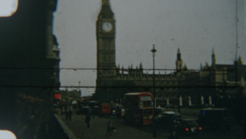 A nostalgic 8mm film from 1960s London captures an iconic view of Big Ben and the Houses of Parliament, with classic red double-decker buses and historic cars navigating the busy streets