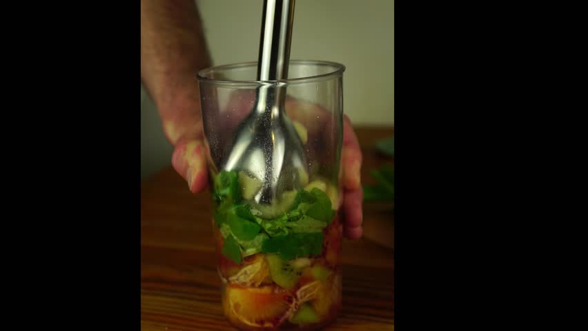 Fruits and green vegetables including orange apple spinach and kiwi being blended in clear cup ingredients swirl and break down into colorful smoothie healthy food concept