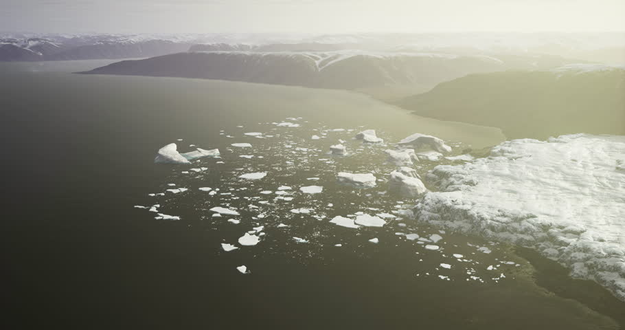 A breathtaking expanse of floating icebergs is illuminated by gentle sunlight along a rugged coastline with snow capped mountains in the background during winter.