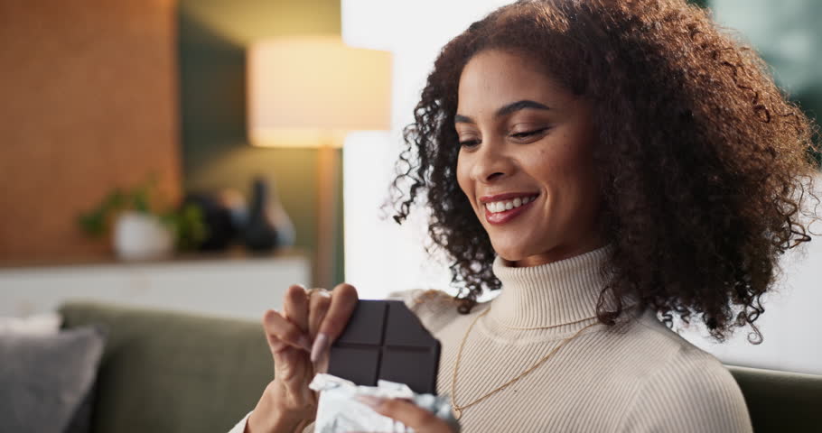 Home, relax and woman eating chocolate bar, taste and enjoy snack with happiness, flavor and smile. Apartment, person and girl on couch, sweat treat and sugar with dessert, comfort food and candy