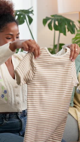 Happy, black woman and folding laundry with basket for housekeeping, washing or cleaning on sofa at home. Female person, housekeeper or cleaner with tshirt or clothing for hygiene or organizing