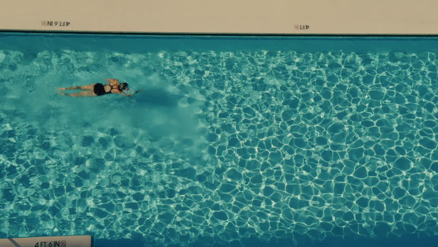 Woman swimming in blue water of the pool on a hot summer day. Above view