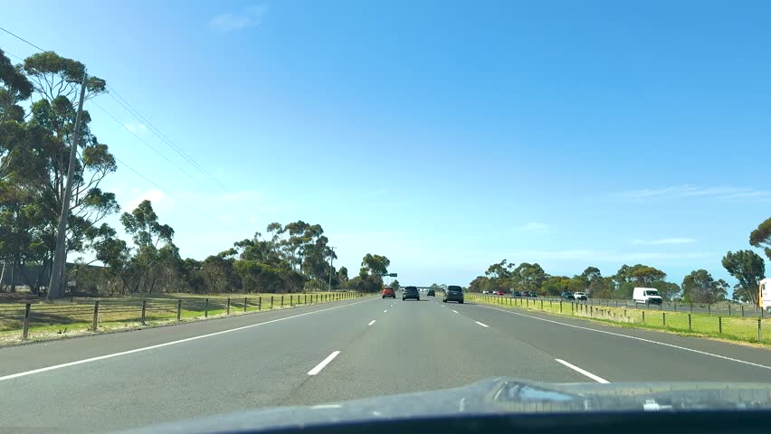 A scenic drive on Great Ocean Road with clear skies, lush greenery, and smooth asphalt, captured in bright daylight