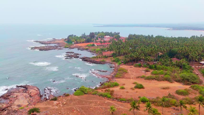 Drone view sea isle with stony fringe and palm trees, Aerial shot large ocean near jagged island, Forest merging along bay line, Seaside cottages stand beside deep lagoon, Foliage joins rough land