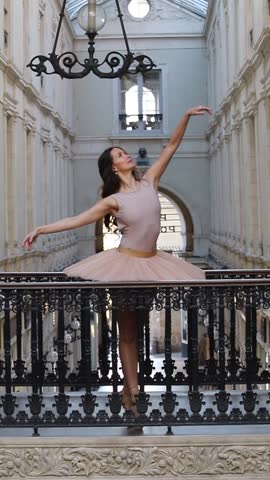 Ballet dancer in a soft pink tutu poses gracefully on pointe inside a vintage shopping gallery with ornate architecture and arches. 