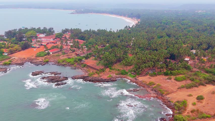 Aerial shot large ocean near jagged island, Drone view sea isle with stony fringe and palm trees, Forest merging along bay line, Seaside cottages stand beside deep lagoon, Foliage joins rough land