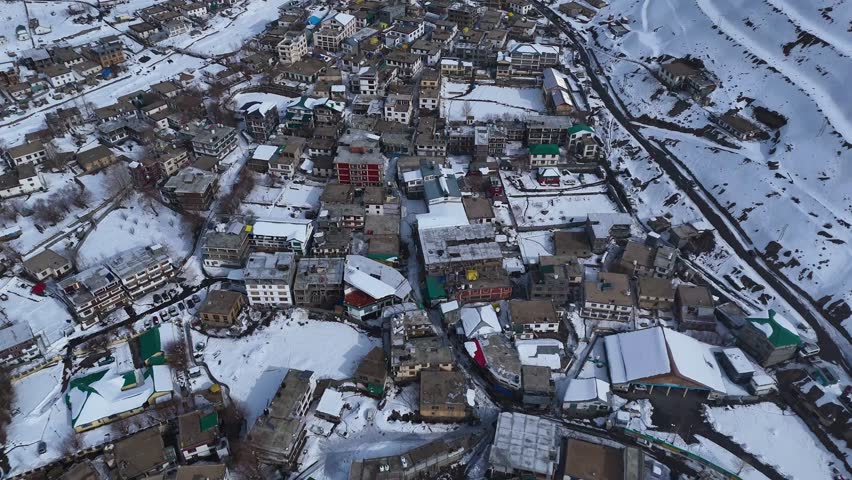 Aerial drone shot of Kaza town under a thick blanket of snow, where the surrounding barren mountains contrast against the pristine white landscape, creating a dramatic winter scene.