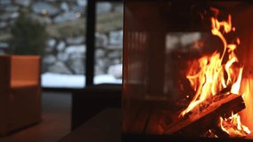 A warm fireplace with flickering flames is in focus, set against large windows revealing a snowy alpine landscape with rocky terrain and sparse greenery. - Powered by Shutterstock - Get 15% off with code: PIKWIZARD15