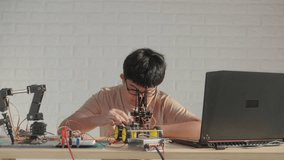 Asian teenage boy connecting wires to circuit board of robotic car with robotic arm at home, STEM education, robotics, and coding for young engineers. - Powered by Shutterstock - Get 15% off with code: PIKWIZARD15