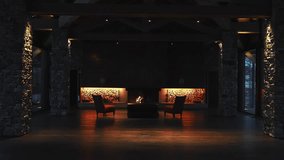 Cozy hotel lounge with a central fireplace, red armchairs, stone walls, and snow covered trees visible through large windows in the background. - Powered by Shutterstock - Get 15% off with code: PIKWIZARD15