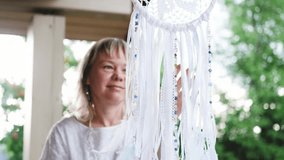 Portrait of a cute young woman in a white dress with a dreamcatcher. The craftswoman made the dreamcatcher herself with white feathers and ribbons. The dreamcatcher sways in the wind. The woman smiles - Powered by Shutterstock - Get 15% off with code: PIKWIZARD15