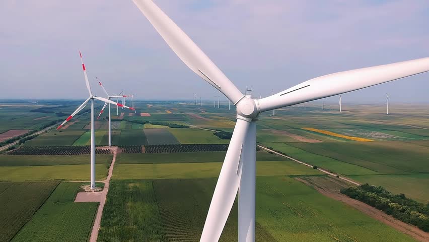 Wind Turbine Spinning Smoothly at Wind Farm - Drone Point Of View. Wind turbines rotates in agricultural landscape. Investing in renewable energy projects. Wind turbines producing electricity.
