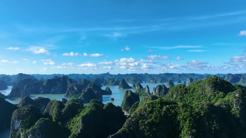 Cinematic drone capture of towering green karsts scattered across Halong Bay’s calm, jade waters, creating a stunning panorama that blends serenity, adventure, and the timeless beauty.