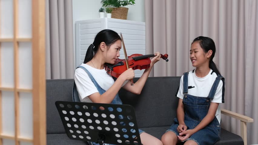 Two cute Asian girls playing violin together at home as favorite activity