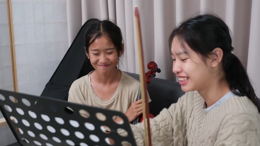 Little Asian girl and older sister playing violin together during school break