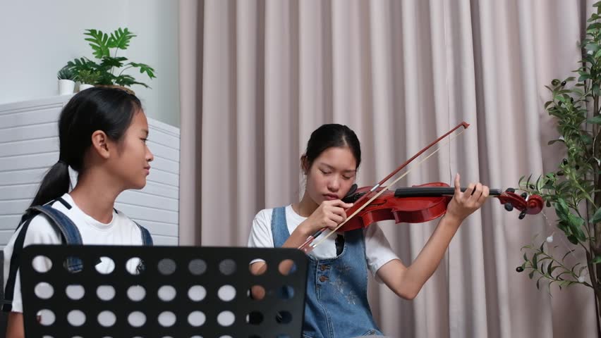 Two cute Asian girls playing violin together at home as favorite activity