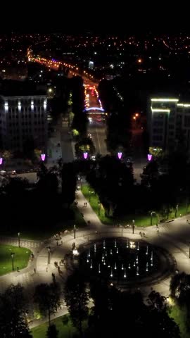 Aerial night illuminated square and streets near Derzhprom, speedup flying forward to descent with bridge in Kharkiv city, Ukraine