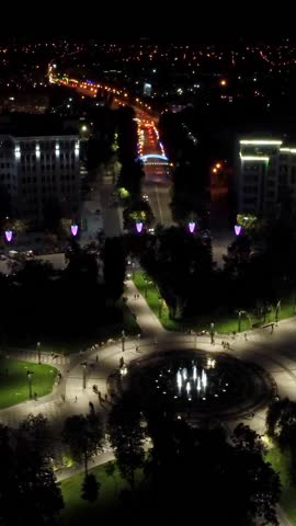 Aerial night illuminated square and streets near Derzhprom, flying forward to descent with bridge in Kharkiv city, Ukraine