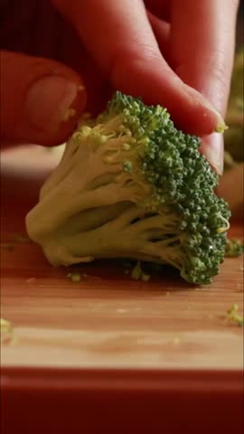 woman's hands carefully slicing fresh broccoli florets on a wooden cutting board