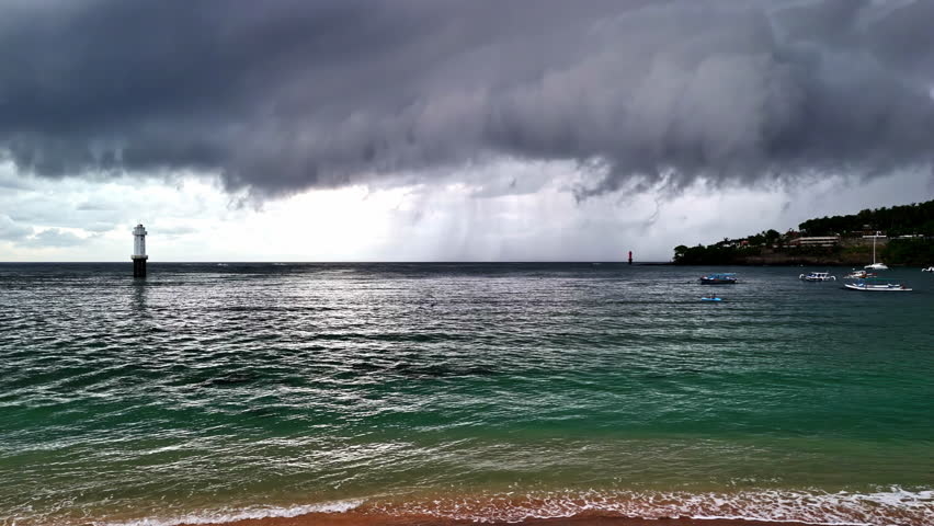 A pedestal shot of Senggigi Beach during a storm, with white boats gently bobbing in the water under dark, stormy skies.