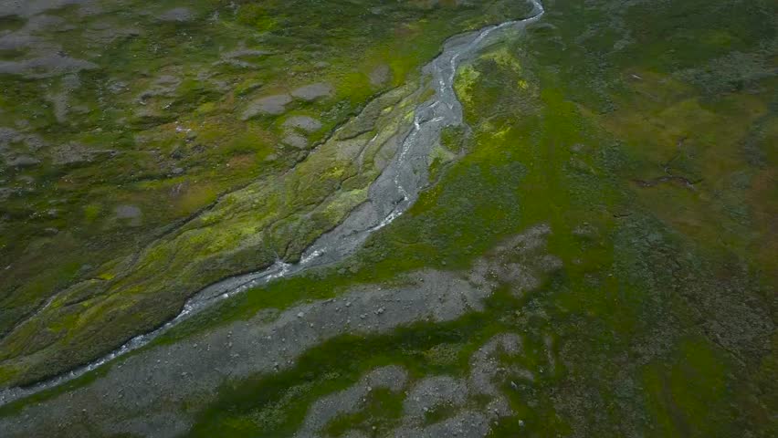 Aerial drone footage video view slowly gliding and flying over green mossy and grassy rocky landscape in Sweden that has a small narrow river flowing on it with white water, foam abd bubbles.