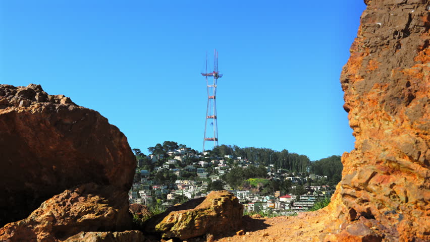 View Of Sutro Tower Over San Francisco Hillside In California, Framed By Rock Formations Against Clear Blue Sky. wide static shot