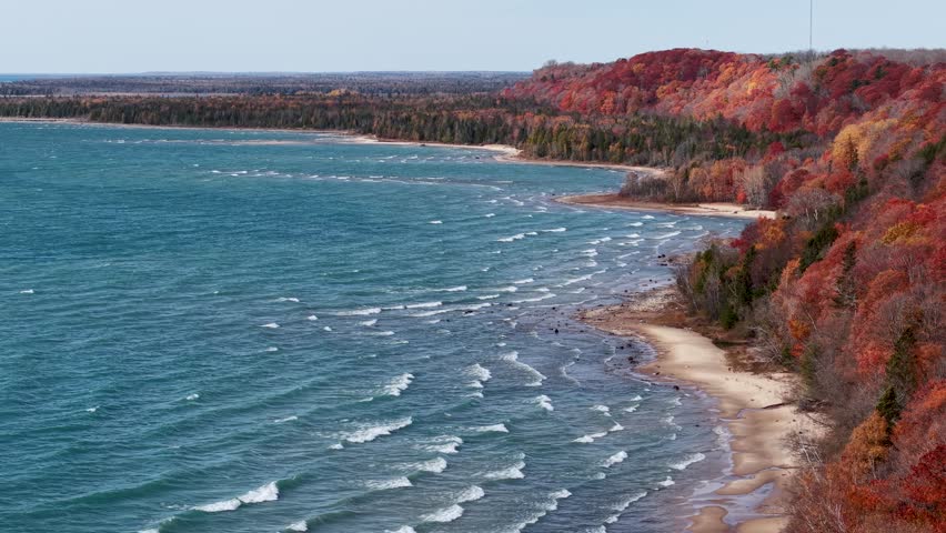 Aerial view of Lake Michigan shoreline in autumn with waves lapping against a colorful forested bluff