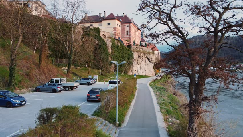 Aerial drone view of Dürnstein in the Wachau Valley in Lower Austria, showcasing terraced vineyards, Danube River, historic medieval villages, lush landscapes of UNESCO World Heritage during sunset.