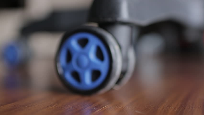 Dusty office chair wheel spinning, accumulating debris on hardwood flooring