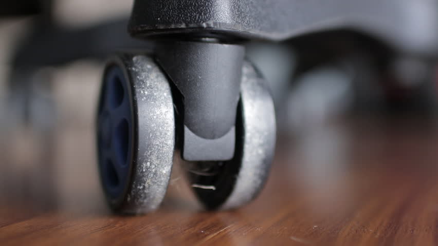 Dusty office chair wheel spinning, accumulating debris on hardwood flooring