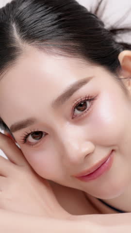Vertical footage beautiful young Asian woman with healthy facial skin isolated over white background for skincare commercial product advertising. Slow motion shot.
