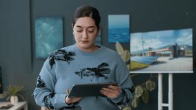 Portrait of young female engineer using digital tablet, then smiling at camera while standing in modern office with renewable energy presentation on screen in background - Powered by Shutterstock - Get 15% off with code: PIKWIZARD15