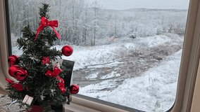 Christmas tree with red bows is sitting on a table at train snow. The window and the view outside is of a snowy landscape in train restaurant dining car railroad transit connection on ground - Powered by Shutterstock - Get 15% off with code: PIKWIZARD15