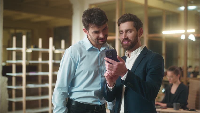 Happy businessmen colleagues friends male business partners guys fellows Caucasian men funny laughing together use mobile phone in office break humor meet friendship laugh smartphone message good news