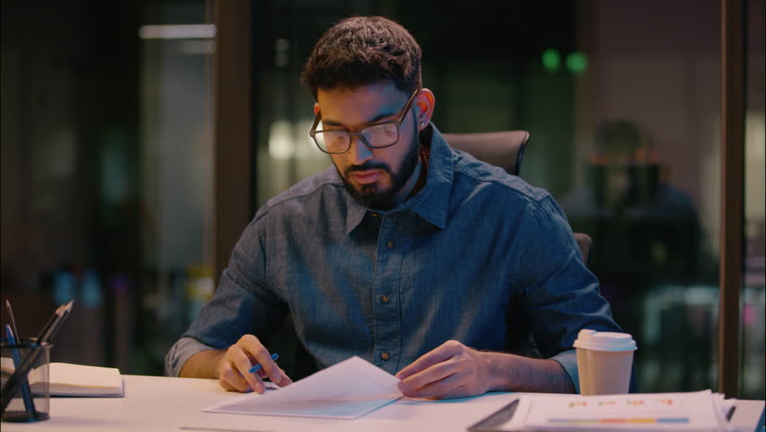 Indian businessman guy male entrepreneur writing document sign contract business deal on table in dark night office overwork Arabian man employee manager ceo write notes bank insurance loan paperwork