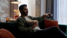 Caucasian bearded joyful man business male businessman guy homeowner buyer client customer falling on sofa couch relaxing eating popcorn unhealthy snack watching TV television using controller at home - Powered by Shutterstock - Get 15% off with code: PIKWIZARD15