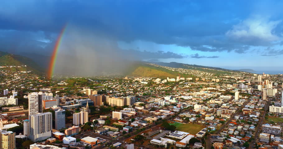 Heavy rain fall from the dark cloudscape on the green mountain. Amazing bright rainbow appears over the city. Drone footage above Honolulu, Oahu, USA. Aerial perspective.