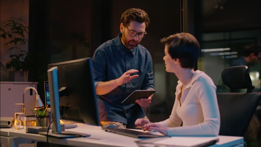 Caucasian business man woman co-workers teamwork at evening night office girl guy working together commerce bitcoin trading computer professional mentor coach consult help businessman businesswoman