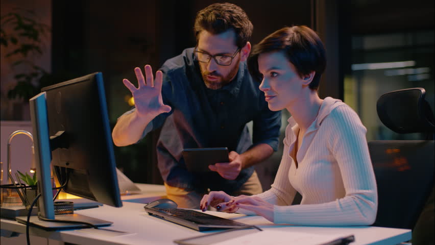 Caucasian business man woman co-workers teamwork at evening night office girl guy working together commerce bitcoin trading computer professional mentor coach consult help businessman businesswoman