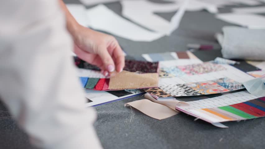 Close up of hand carefully lifting various colorful fabric samples during creative fabric selection process, showcasing vibrant materials, different textures, and fashion design development scene