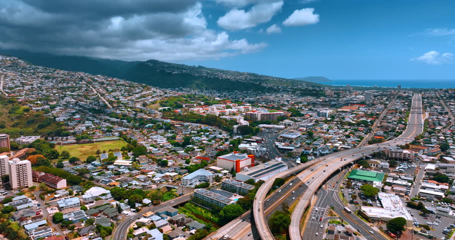 Vast dense cityscape of sunny Honolulu, Hawaii, USA. Grey dramatic cloudscape rolls on the city from mountains. Aerial perspective.