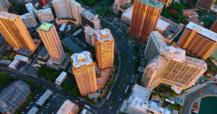 High-rise buildings lit with orange light of sunset. Aerial perspective on the city above the roads. Honolulu, Hawaii, USA.