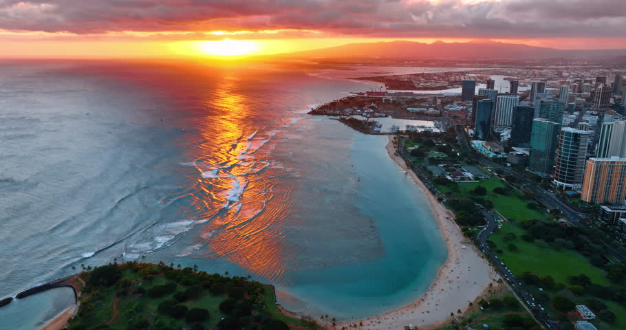 Orange setting sun reflecting on the waterscape of the Pacific Ocean at the coast of Waikiki, Honolulu, Hawaii, USA. Amazing sunset lighting the sky. Aerial view.
