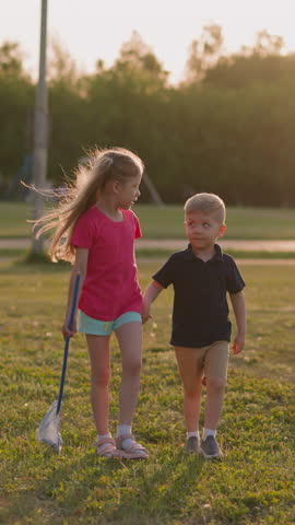 Elder sister preschooler and toddler brother walk along playground at sunset slow motion. Cute friends play together in summer. Children in park