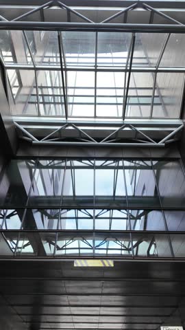 Upward view of a modern building’s interior featuring a steel truss structure, large glass windows, and a skylight ceiling.
