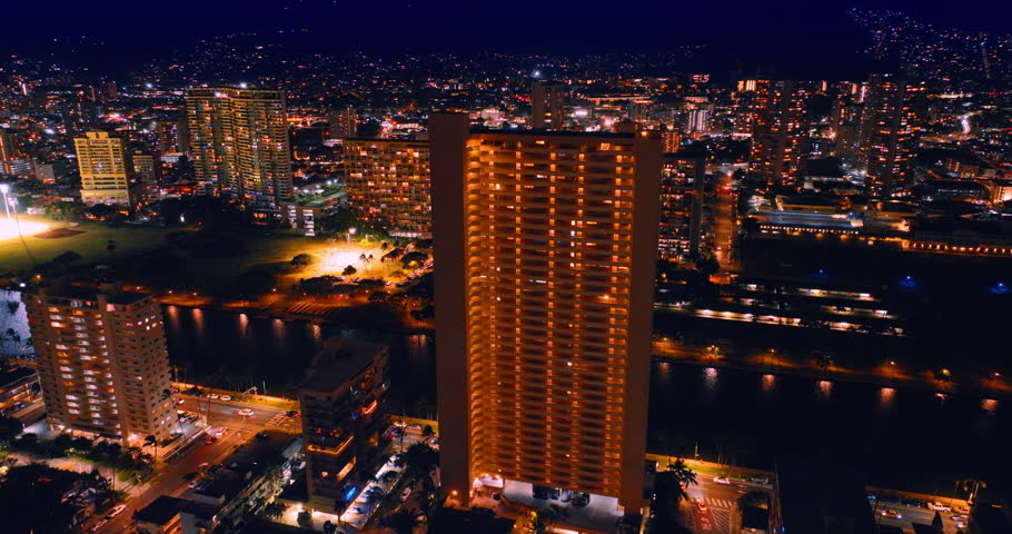 Flying over the Ala Wai Canal to the well-lit cityscape of Honolulu, Hawaii, USA. Dazzling lights of the city at night.
