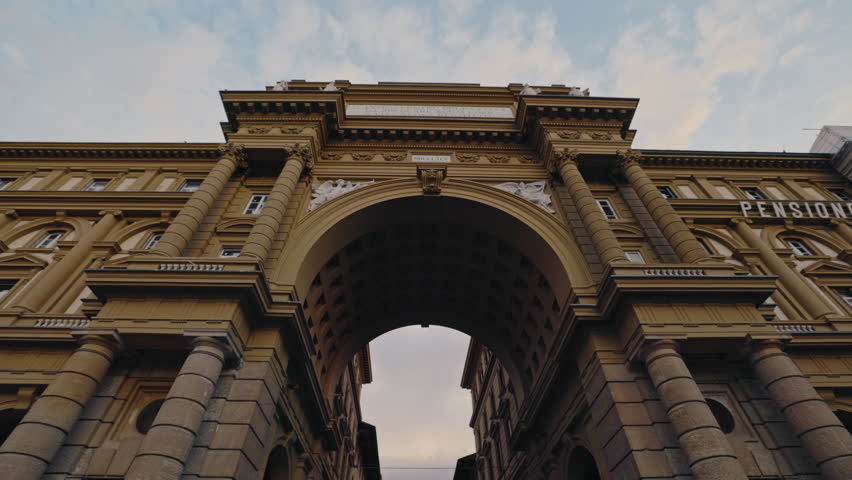 FLORENCE, ITALY - AUGUST 15 2024: Historical Triumphal arch on Piazza della Repubblica under sky with light clouds. Gorgeous architectural monument on old city square low angle shot. European tour
