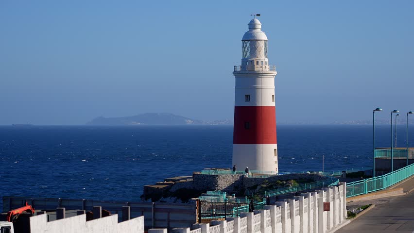 Europa Point Lighthouse stands on a cliff overlooking the Strait of Gibraltar, guiding ships near Gibraltar, United Kingdom, with Morocco in the background