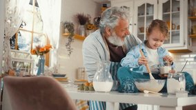 A cute 5-year-old boy is sitting on the table and laughing, having fun with his grandfather while preparing pancake batter at home in the kitchen. - Powered by Shutterstock - Get 15% off with code: PIKWIZARD15