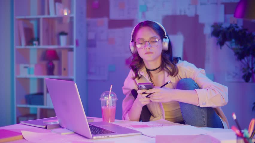 Gen Z Lifestyle, Digital Multitasking, Neon Mood. Teen Girl Draws While Listening Music and Watching Laptop Screen. Personal Expression in Creative Chaos of Modern Youth in Neon Light
